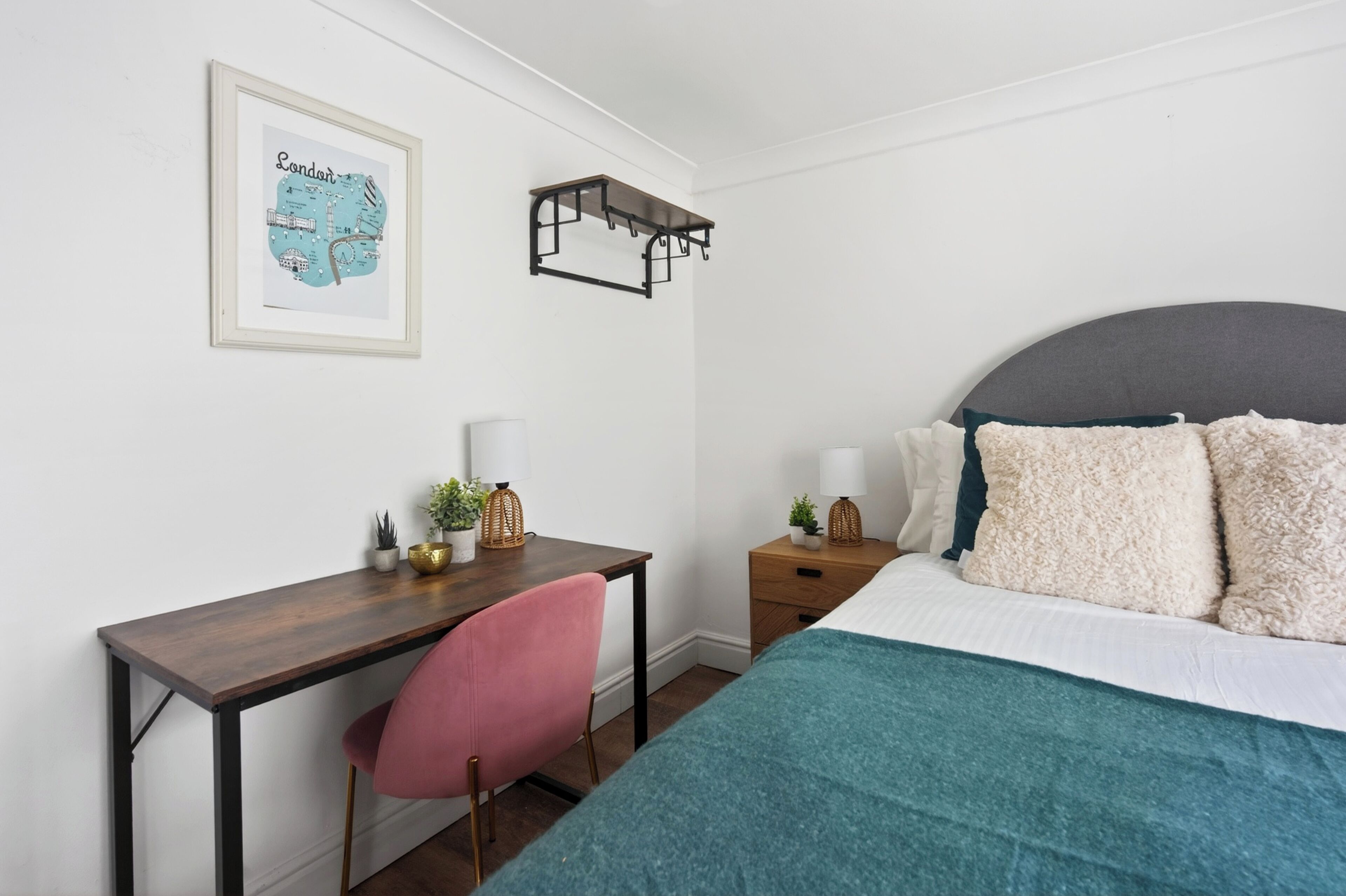 A bedroom with a bed, a desk, a chair, a nightstand, a framed map, and a hanging light fixture.