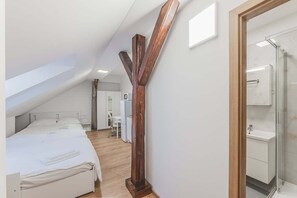 Une chambre avec un plafond en pente, un élément décoratif en bois, un lit, un bureau et une salle de bain avec une douche en verre.