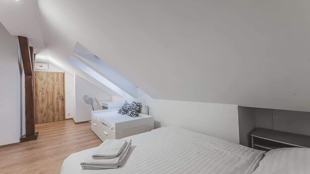 Une chambre avec un plafond en pente, un lit, une table de chevet et une porte en bois.