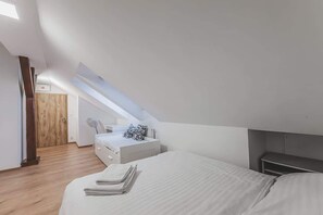 Quarto com teto inclinado, uma cama, mesa de cabeceira e porta de madeira.