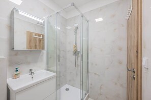 Une salle de bain moderne avec une douche à parois de verre, un lavabo blanc et une porte en bois.