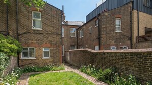 Un estrecho callejón entre dos edificios de ladrillo, con un pequeño espacio cubierto de césped y flores.