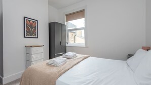 Un dormitorio con cama, armario, mesita de noche, ventana con persianas y un cuadro colgado en la pared.