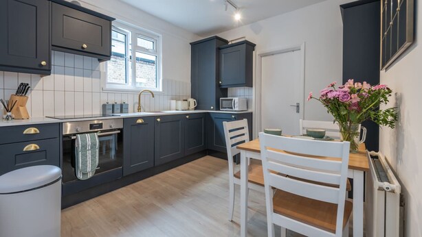 Una cocina moderna con armarios oscuros, una mesa de comedor de madera y una ventana.