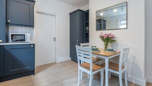 Cocina compacta con armarios oscuros, un microondas y un comedor con sillas blancas y una mesa.
