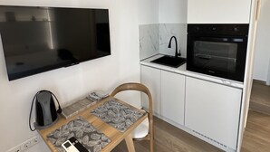 Cocina compacta con horno empotrado, televisor de pantalla plana y comedor con mesa y silla.
