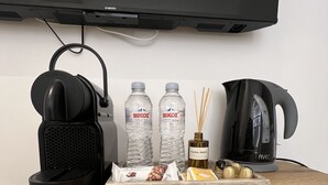 Una mesa de madera con un altavoz negro, dos botellas de agua, un aroma floral, una tetera negra y una bandeja con aperitivos.