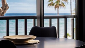 Ein Tisch mit geflochtener Unterlage und einer Schale, ein Stuhl und Blick auf den Ozean durch große Fenster.