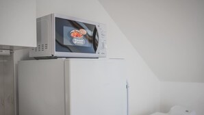A white refrigerator with a microwave on top, a white bed, and a white wall. - Andel, Smichov Flat, Fresh Bath, port AC, Kitchen (Praha 5)