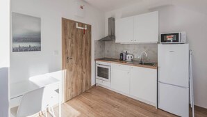 A compact kitchen with white cabinets, a wooden door, a microwave, a kettle, and a refrigerator. - Andel, Smichov Flat, Fresh Bath, port AC, Kitchen (Praha 5)