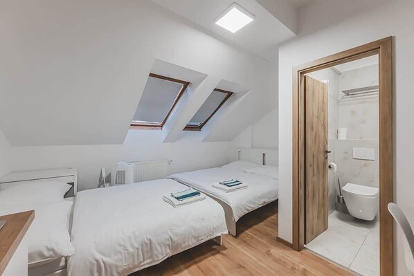 A modern bedroom with two beds, a skylight, a wooden door, and a view of the bathroom. - Andel, Smichov Flat, Fresh Bath, port AC, Kitchen (Praha 5)