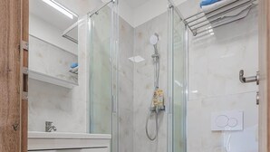 Ein modernes Badezimmer mit einer gläsernen Duschkabine, einer weißen Toilette und einem Waschtisch mit Schubladen.