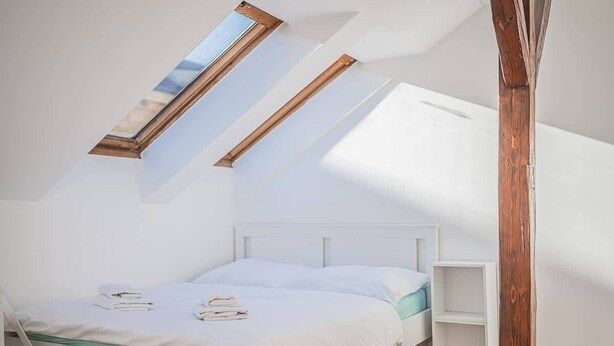 Ein Schlafzimmer mit schrägem Dach, einem Oberlicht, einem Bett und einem Holzbalken.