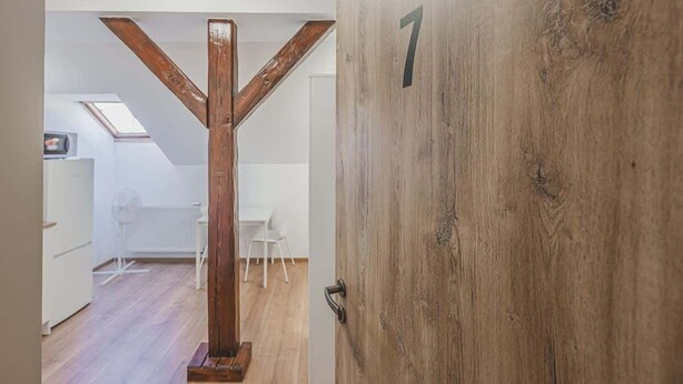 Eine Holztür mit Hausnummer, eine Treppe mit hölzernem Geländer und ein weißer Stuhl in einem Raum mit Holzboden.