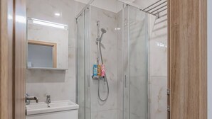 Moderni kylpyhuone, jossa on lasiseinällä varustettu suihku, valkoinen pesuallas ja wc.