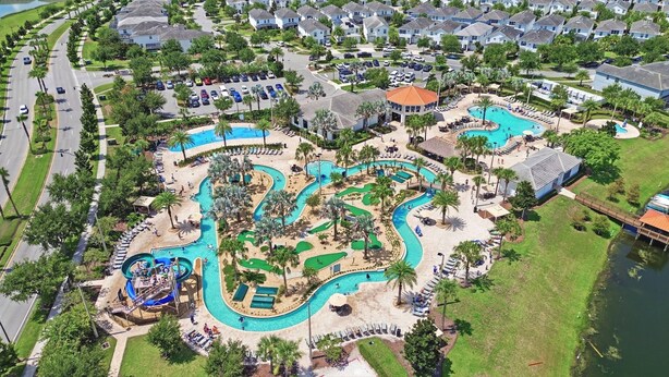 Une vue aérienne d’un complexe hôtelier doté de plusieurs piscines, d’un toboggan aquatique et d’un pont enjambant une étendue d’eau.