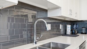 Une cuisine moderne dotée d’un évier en acier inoxydable, de meubles blancs et d’un pare-feu en carreaux gris.