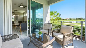 Un balcon agrémenté de meubles en osier, d’une table en verre et offrant une vue sur un lac.