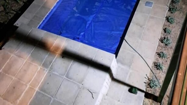 Piscina retangular com cobertura azul, rodeada por um terraço ladrilhado com detalhe decorativo.
