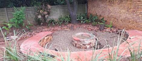 A circular garden area with a central fire pit, surrounded by a brick border and various plants.