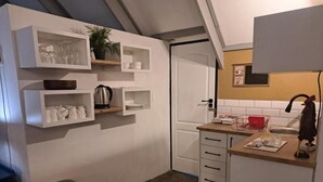 Uma cozinha compacta com armários brancos, uma pia e um balcão com uma chaleira e uma planta.