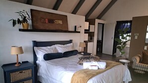 Quarto com cama, mesas de cabeceira, luminária, planta e vista para cozinha.