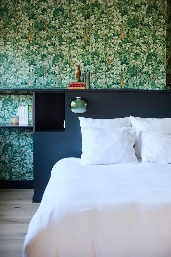 A bed with white bedding, a dark headboard, and a wall with a leafy pattern. - Maison d'Artiste (Ghent)