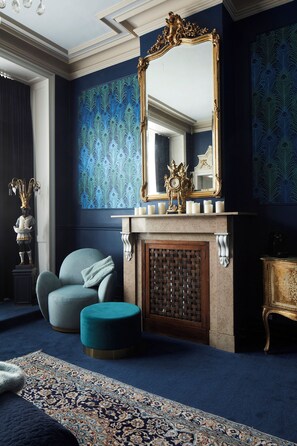 Una habitación con un espejo grande, chimenea, pared con diseño azul y un sillón azul.