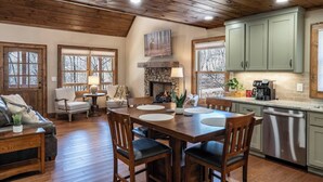 A cozy kitchen with a stone fireplace, wooden dining table, and light green cabinets. - Thyme Out | Hot Tub | 7 Minutes to Blue Ridge (Blue Ridge)