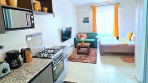 A compact living space with a kitchenette, a sofa, a coffee table, and a TV. - Beautiful Place to Unwind – Executive Studio at Garden City Mall, Garden 237 (Nairobi)