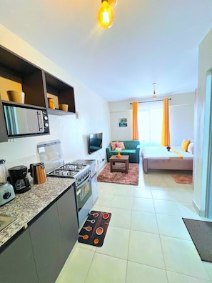 A compact living space with a kitchenette, a sofa, a coffee table, and a TV. - Beautiful Place to Unwind – Executive Studio at Garden City Mall, Garden 237 (Nairobi)