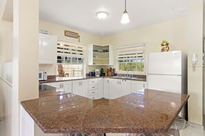 A kitchen with white cabinets, a granite countertop, a refrigerator, and a sign that says 'KITCHEN'. - Palm View 4 - Cozy 2 bedroom apartment in Barbados (Bridgetown)