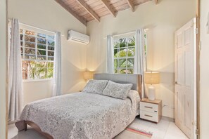 A bedroom with a bed, bedside lamps, a nightstand, a door, and windows with curtains. - Palm View 4 - Cozy 2 bedroom apartment in Barbados (Bridgetown)