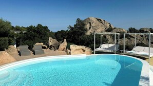 Ein klares, blaues Schwimmbecken mit Liegestühlen und einer Pergola, umgeben von natürlichen Felsformationen und Bäumen.