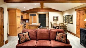 A spacious living area with a red sofa, wooden ceiling beams, a dining table, and a kitchen in the background. - One Bedroom Two Queen Suite 1 Suite (Park City)