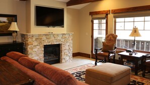 A living room with a stone fireplace, a television mounted above it, a sofa, and a table with chairs. - One Bedroom Two Queen Suite 1 Suite (Park City)