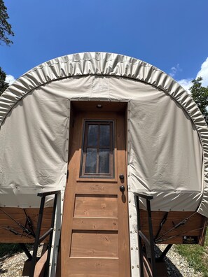 Una porta di legno con una finestra, una struttura simile a una tenda e il nome 'CONESTOGA' sulla porta.