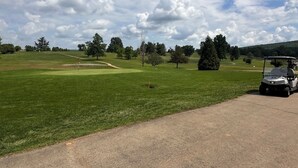 En golfbana med klar himmel, grön gräsmatta och en golfbil.
