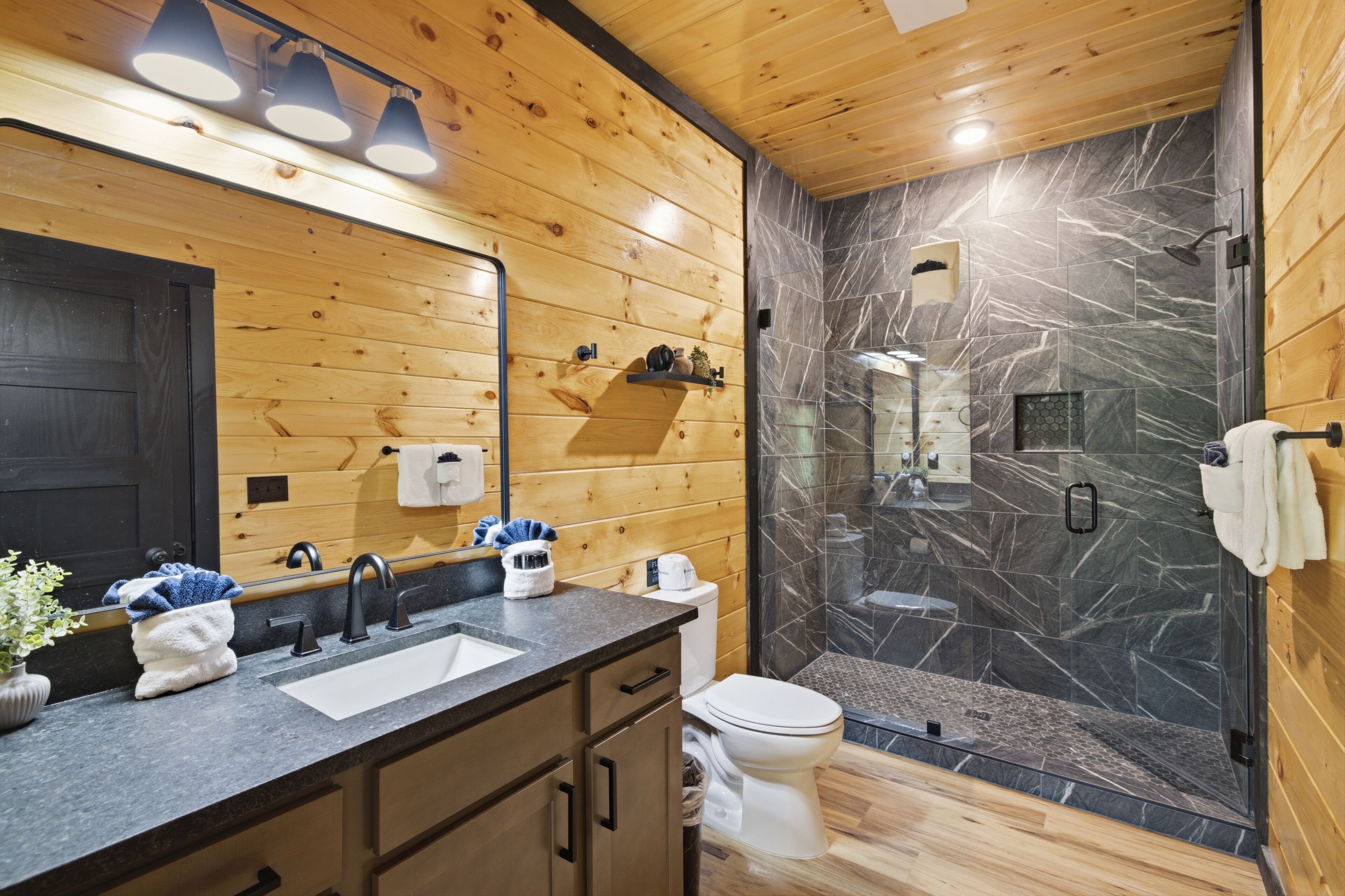 Une salle de bain intérieure au décor en bois, équipée d’un lavabo, d’un miroir et d’une douche.