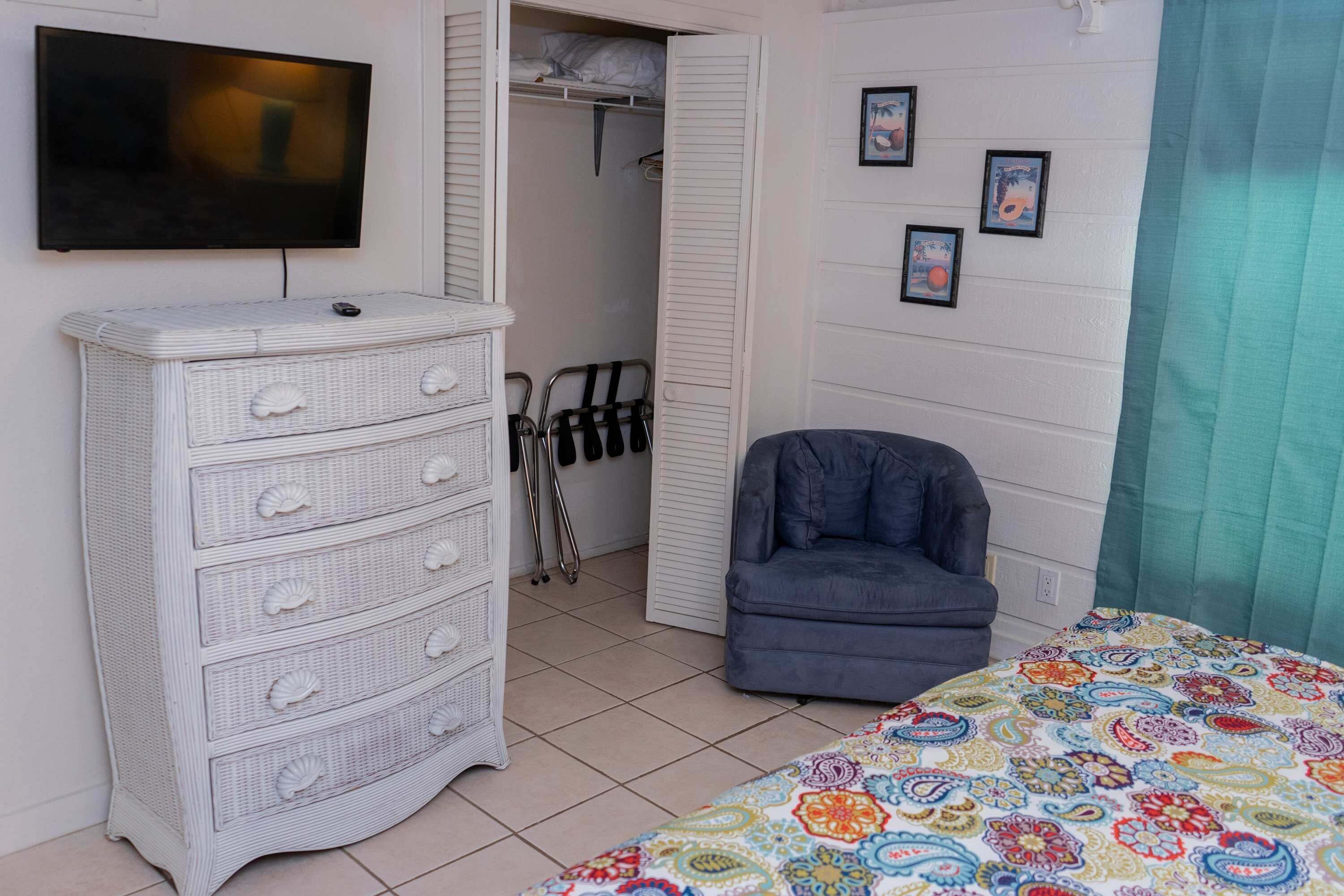 Een slaapkamer met een bed, een ladekast, een stoel, een televisie en een kledingkast.