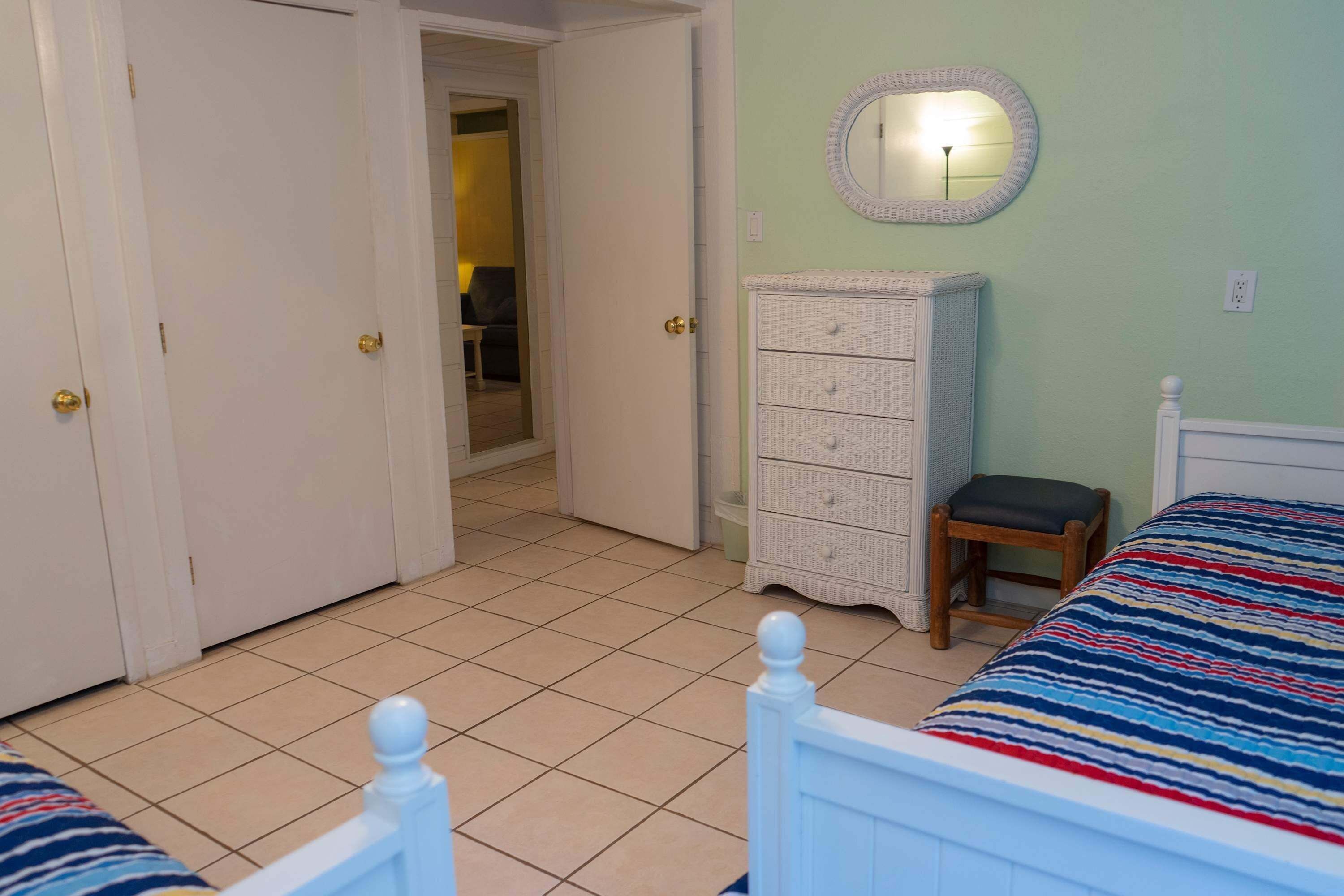 A bedroom with two beds, a dresser, a mirror, and a door leading to another room.