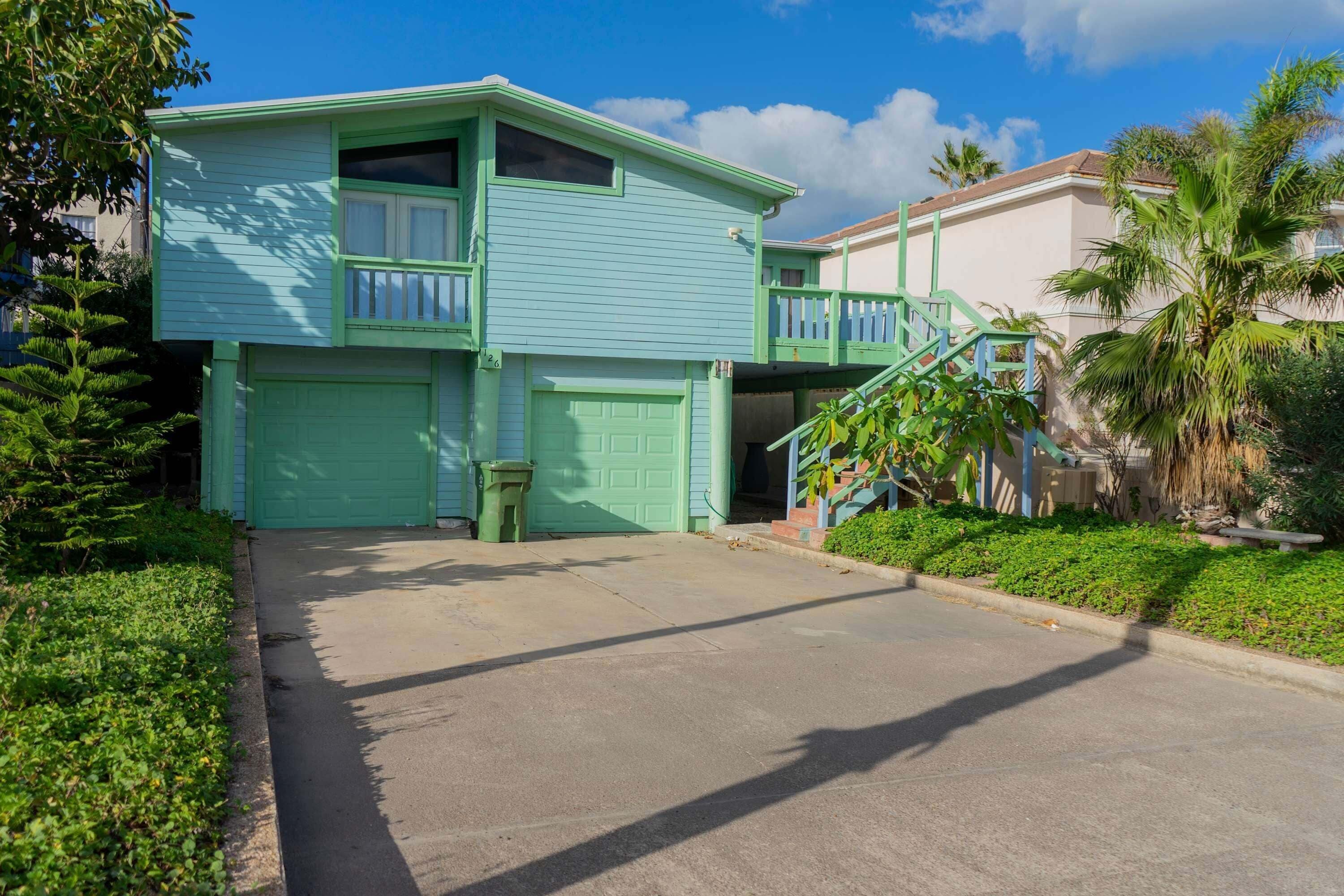 A two-story house with a green exterior, a garage, and a staircase leading to a second level.
