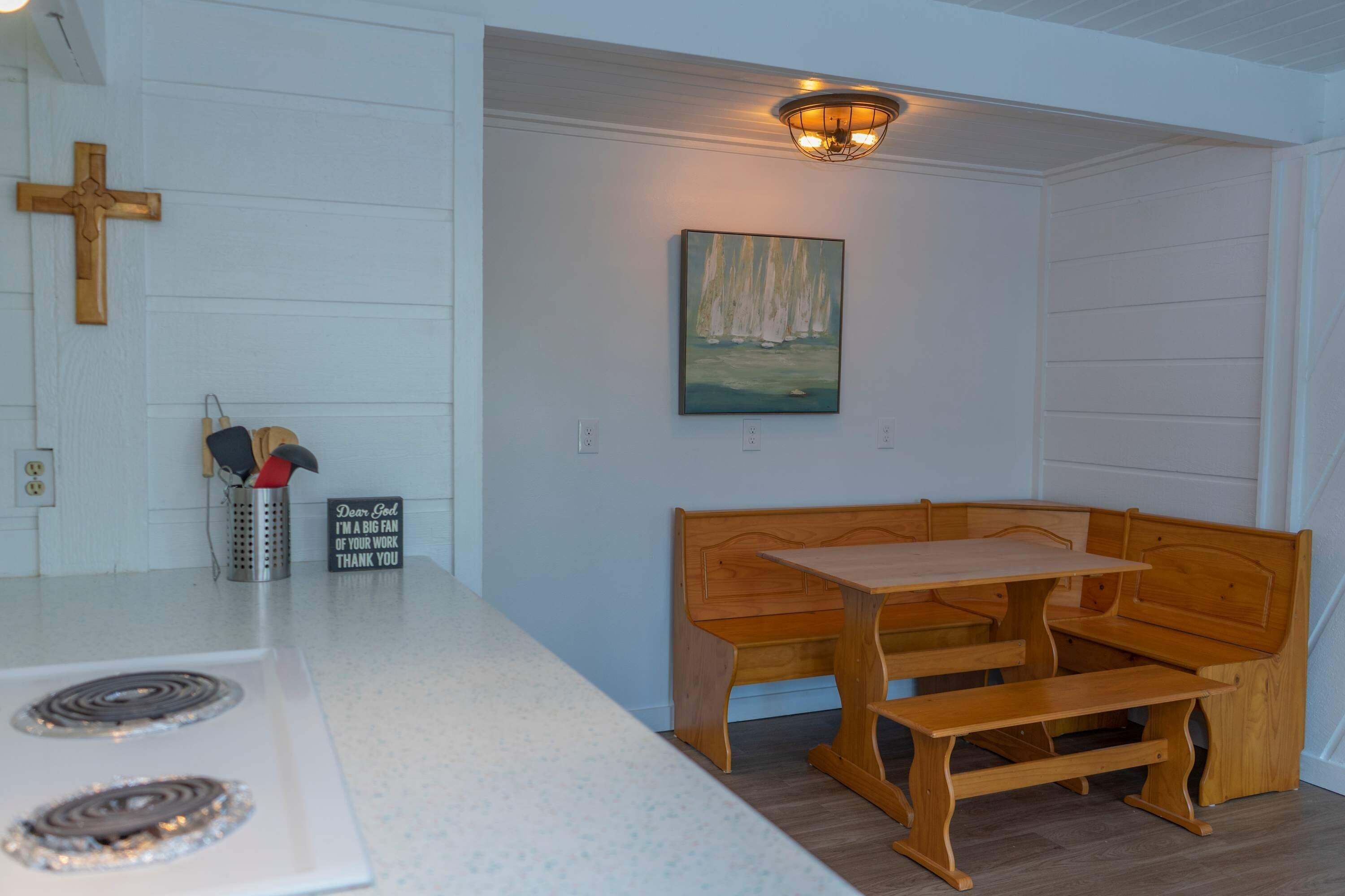 A kitchen with a wooden bench and table, a cross on the wall, and a painting above the bench.
