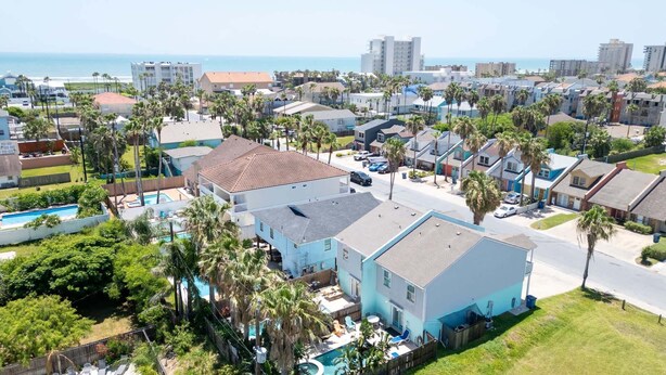 Un quartier résidentiel avec une grande maison dotée d’une piscine, entourée de palmiers et offrant une vue sur l’océan.