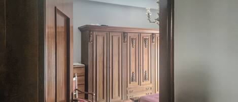 A room with a wooden wardrobe, a chair, and a bed with a pink bedspread.