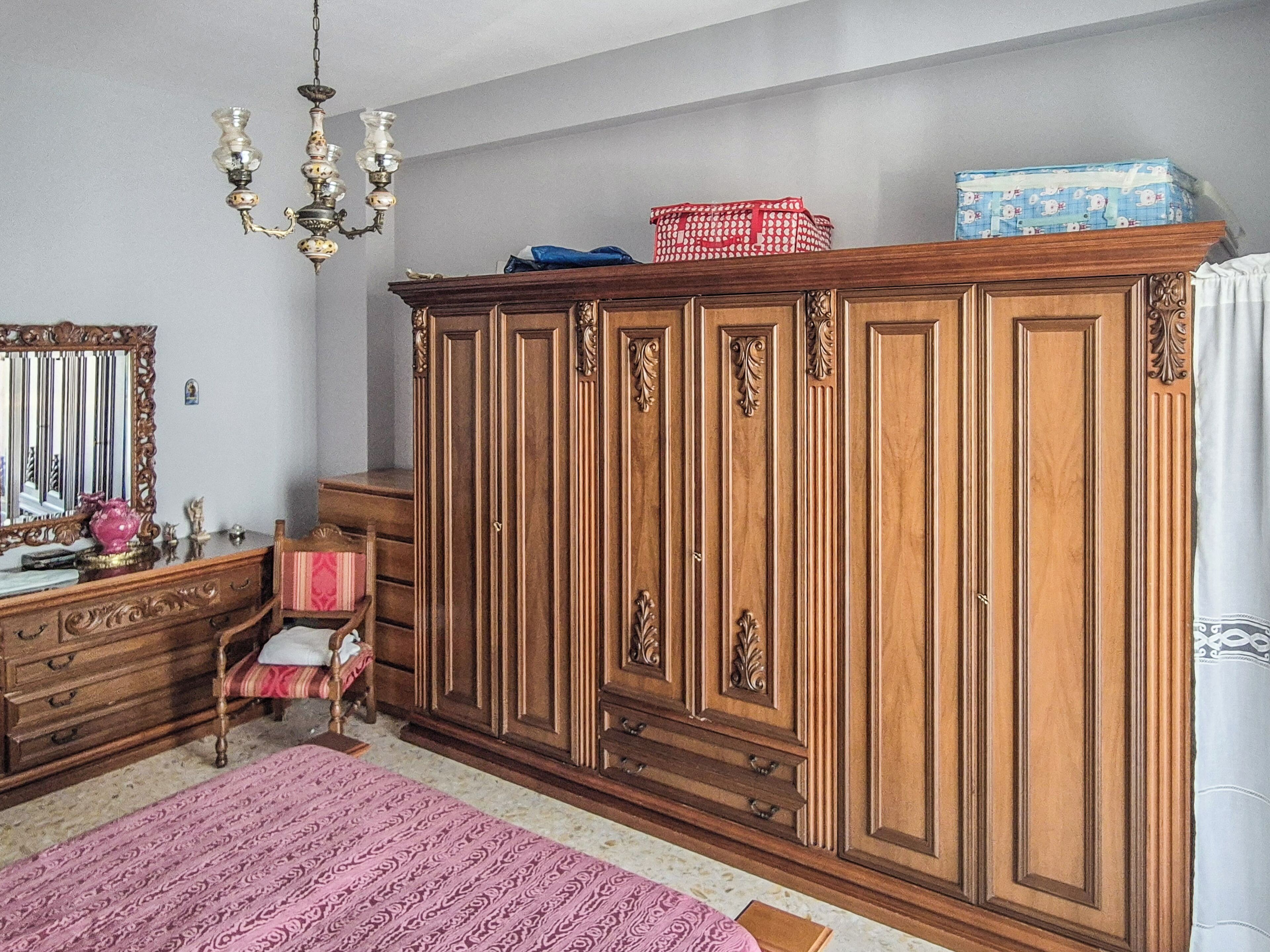 A room with a large wooden wardrobe, a mirror, a chandelier, and a patterned rug.