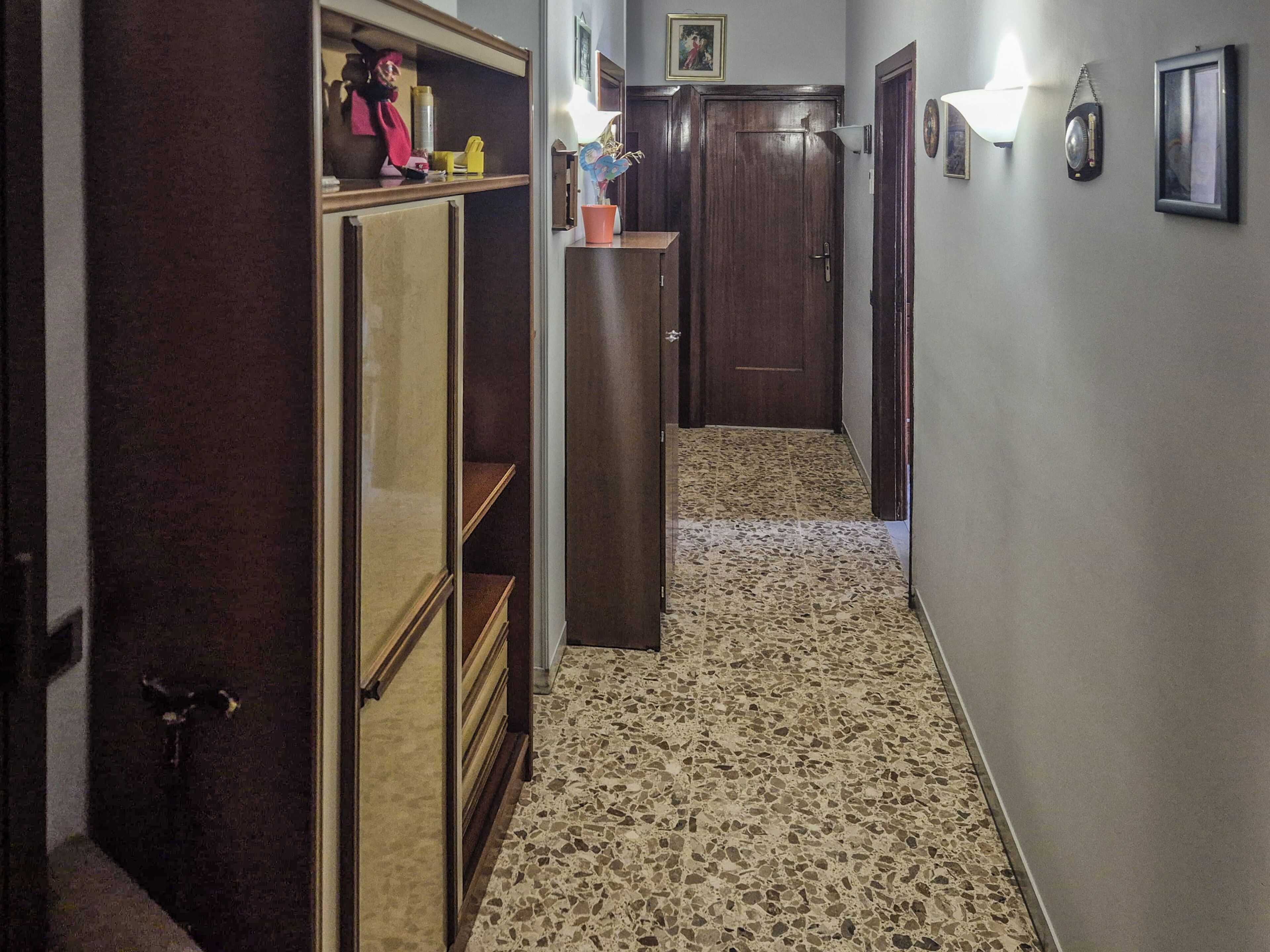 A hallway with a tiled floor, wooden cabinets, and a door.