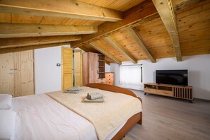 Un dormitorio con techo de madera, una cama con manta beige, un mueble para televisión y un armario.