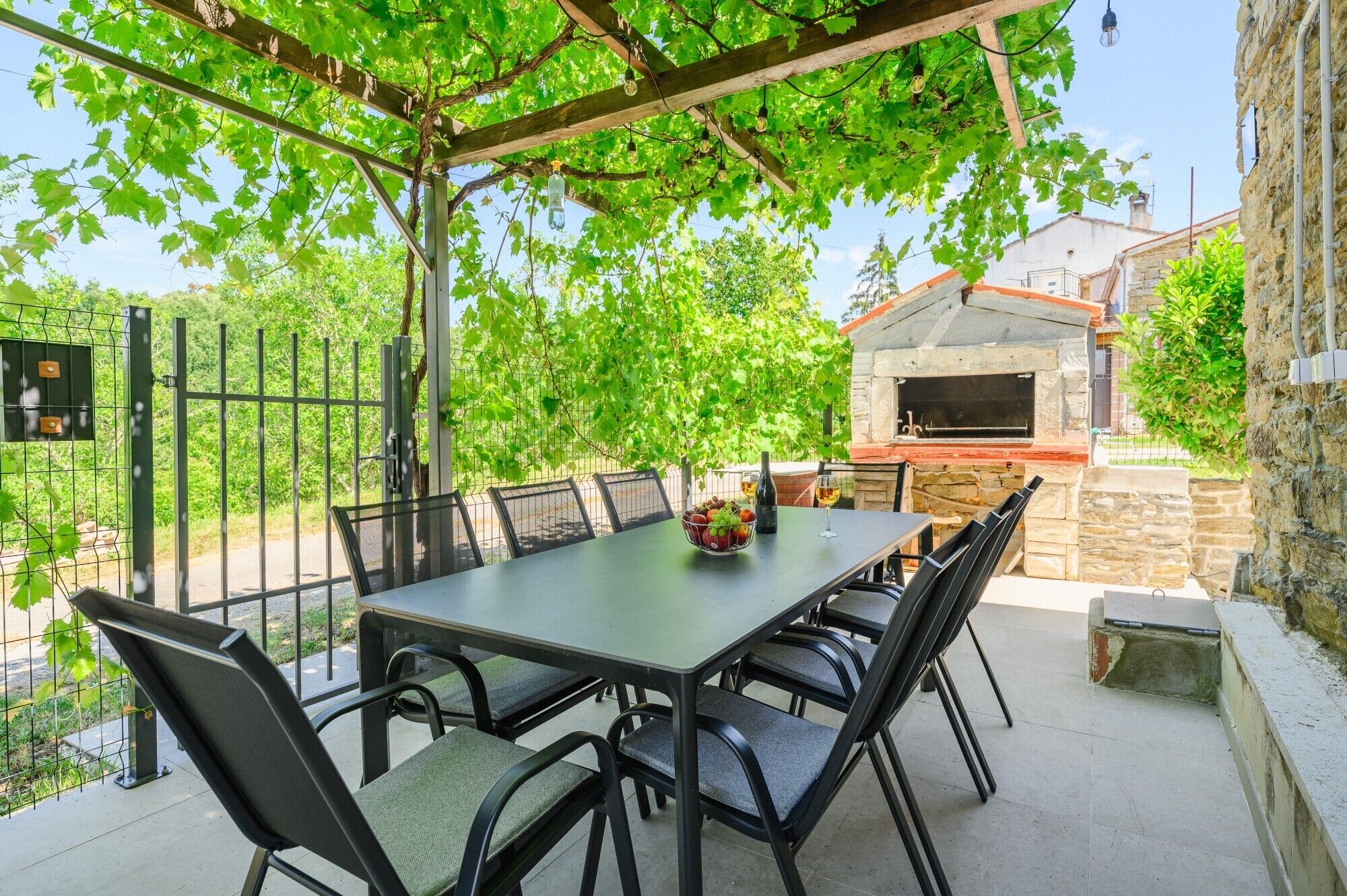 An outdoor patio with a table and chairs, a stone oven, and a pergola with vines.