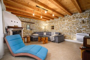 A cozy room with a stone wall, wooden ceiling beams, a blue chair, a gray sofa, and a small table. - Casa Rosina in Šestani - Haus für 4-5 Personen (Zarecje)